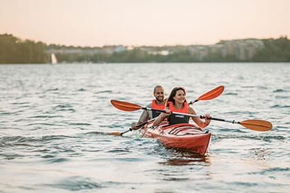 Happy smiling couple paddling a red tandem kayak during a beautiful sunset
