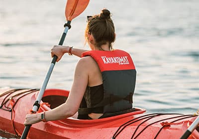 Young woman paddles a red kayak into the sunset.